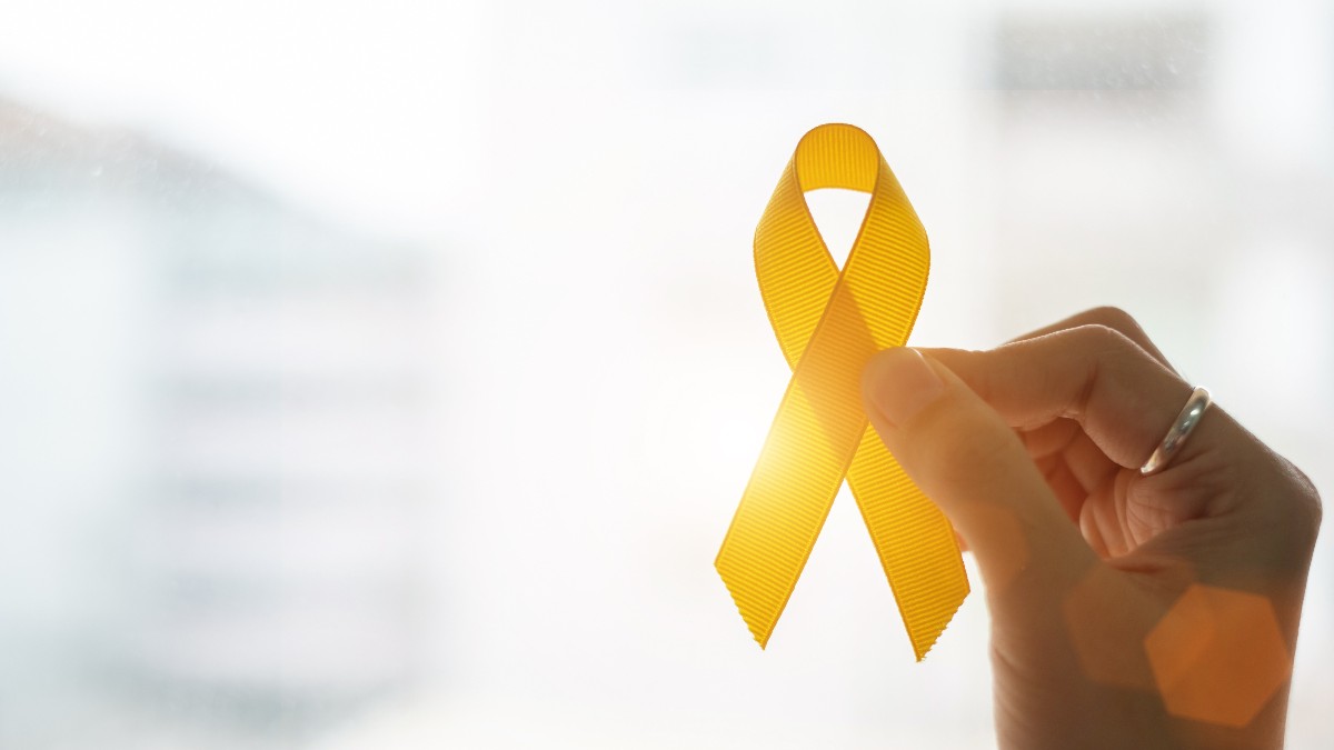 Imaginea prezintă o mână care ține o panglică portocalie, simbol al luptei împotriva cancerului și al solidarității cu pacienții. Lumina caldă din fundal accentuează mesajul de speranță și susținere.