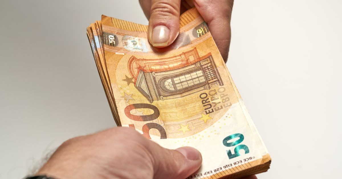 Mâna unui bărbat care ține mai multe bancnote de 50 de euro și le îndreaptă spre o femeie care a pus mâna pe ele