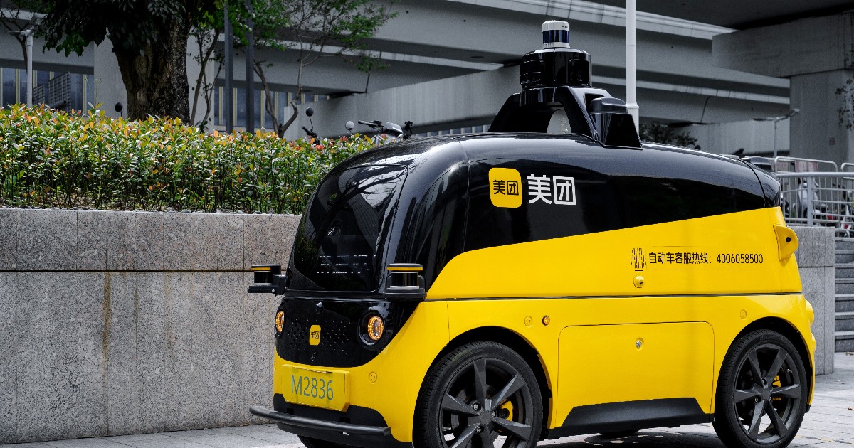 Imaginea surprinde un vehicul autonom de livrare, de mici dimensiuni, care circulă pe o alee urbană din China, fiind echipat cu senzori și camere montate pe plafon. Designul compact, în culori galben și negru, sugerează un robot de livrare destinat deplasării prin trafic pietonal și zone aglomerate din oraș.