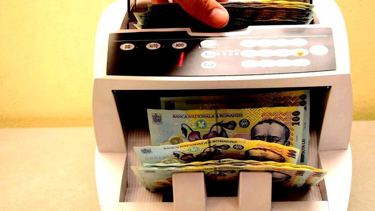 Guvernul a colectat cu 21 de miliarde de lei mai puțin decât și-a propus, iar diferența nu poate fi recuperată până la final de an. Aparat de numărat bani cu teancuri de bancnote în el