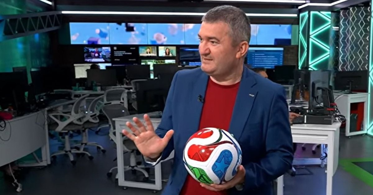 Dorin Chioțea îmbrăcat cu o bluză roșie, sacou albastru, în studioul Euronews România, în timp ce ține o minge de fotbal în mâna stângă, pe 23 iunie 2026