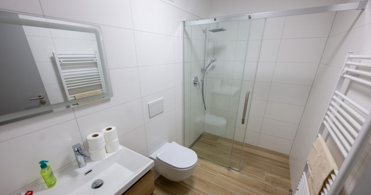 O baie, cu duș, chiuvetă și wc, placată cu faianță albă.