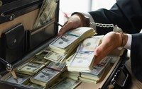 Mâini încătușate ținând un teanc de bani dintr-o servietă neagră