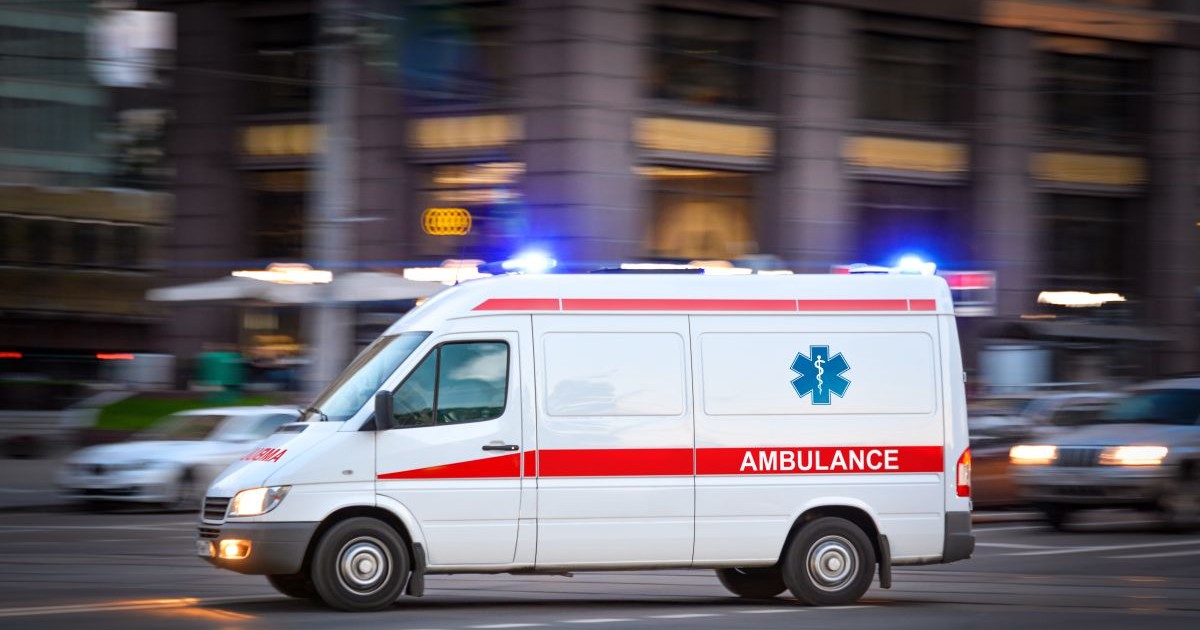 O mașină a Ambulanței în trafic, cu luminile aprinse, într-un fundal neclar.