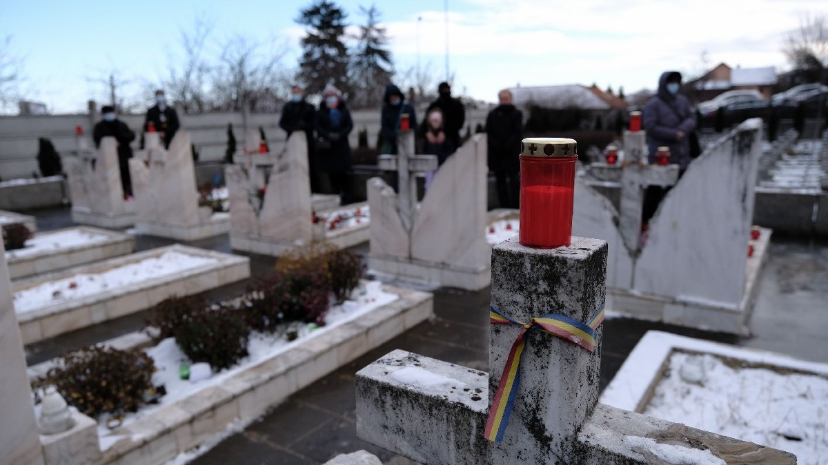 Persoane participa la ceremoniile dedicate comemorarii victimelor evenimentelor din Decembrie 1989, in Cimitirul Eroilor din Cluj, marti, 21 decembrie 2021. O lumânare rosie se vede in prim plan, pe un stalp de care este legat un tricolor.