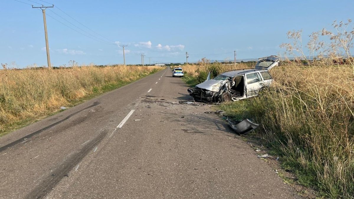 In imagine un drum prin camp, in dreapta se vede o mașină gri distrusa in urma unui accident, o alta masina se poate observa in depărtare, Buzau, august 2025