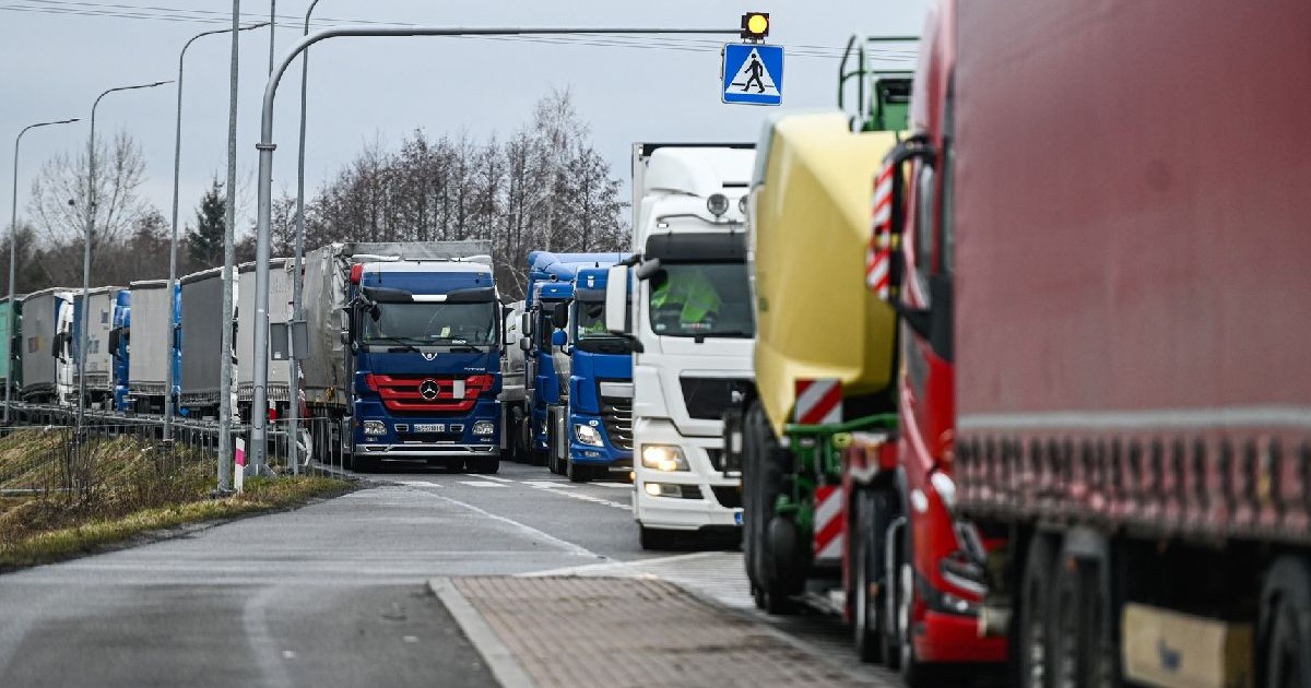 Fotografie cu un ambuteiaj lung pe o autostradă, în care apar diverse camioane, de diferite culori, inclusiv albastru, alb și roșu, într-o zi ploioasă, cu cerul înnorat.