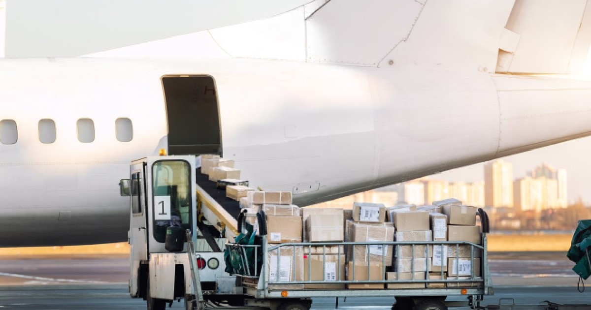 Cărucior de marfă plin cu colete comerciale în fața unui avion de marfă cu turbopropulsor.