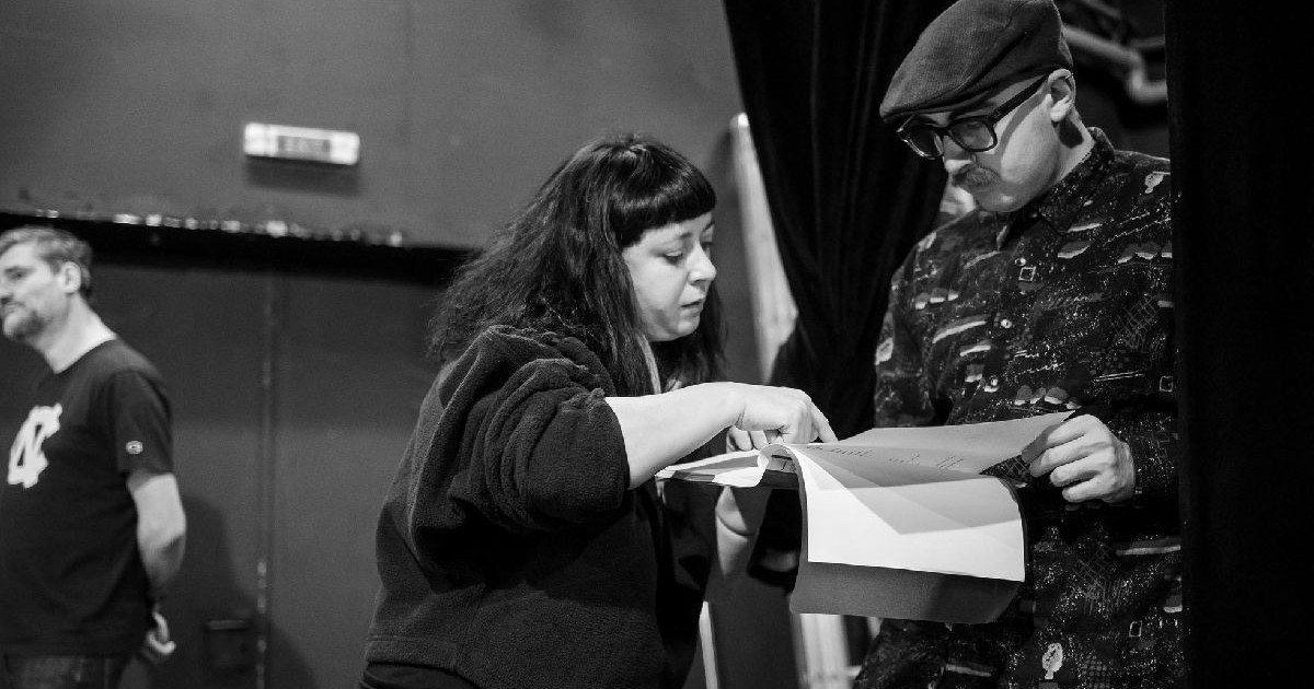 O fotografie alb negru cu regizoarea Alexandra Penciuc citind alături de un alt actor, probabil, scenariu piesei.