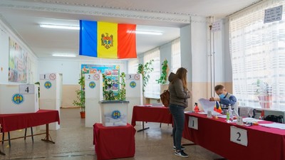 O femeie se află într-o secție de vot în Republica Moldova și așteaptă să fie găsită pe listele electorale de un funcționar, pentru a verifica prezența ei pe lista alegătorilor, înainte de a-i înmâna buletinul de vot