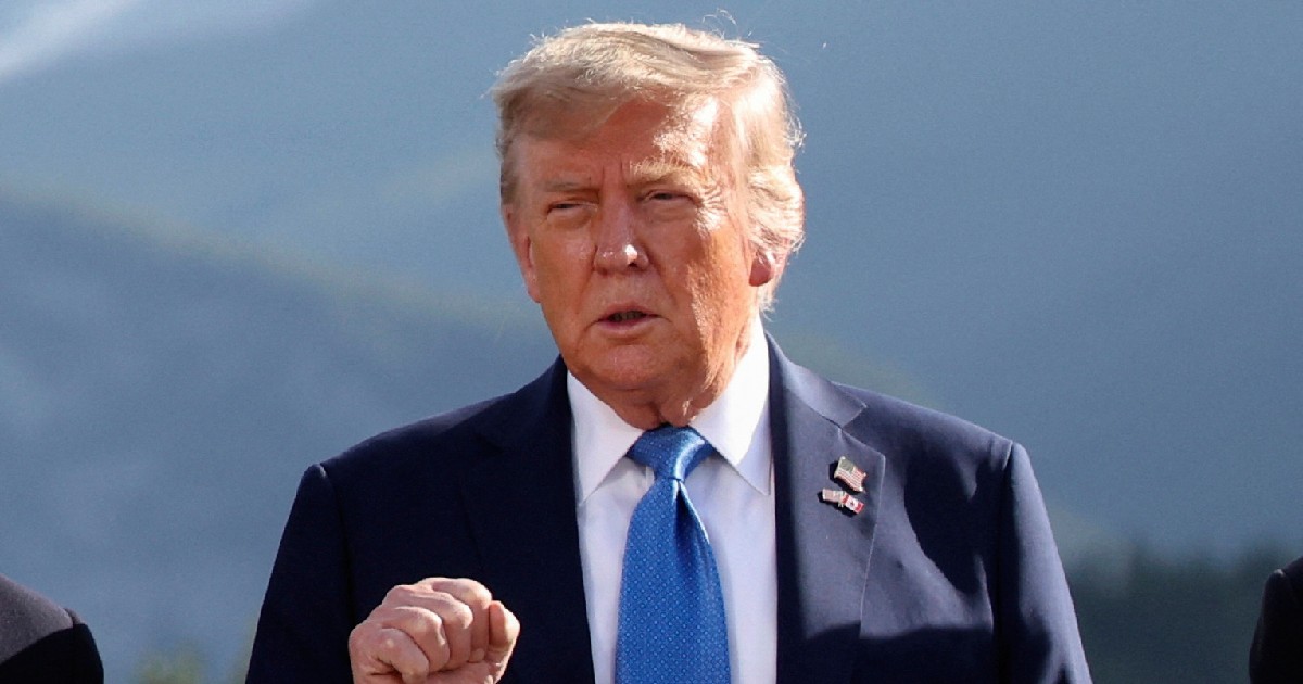 Donald Trump îmbrăcat într-un costum negru, cu o cămașă albă și o cravată albastră, ridicând pumnul în aer, în timpul unui discurs