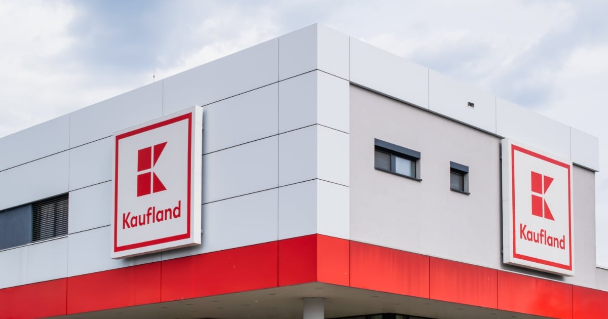 În imagine este surprinsă fațada unui magazin Kaufland. Clădirea are un design modern, cu panouri albe și gri, iar în partea superioară se află logo-ul Kaufland pe fundal roșu, afișat de două ori.