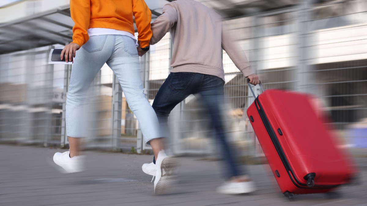 Două persoane care aleargă cu o valiză roșie la intrarea unui aeroport