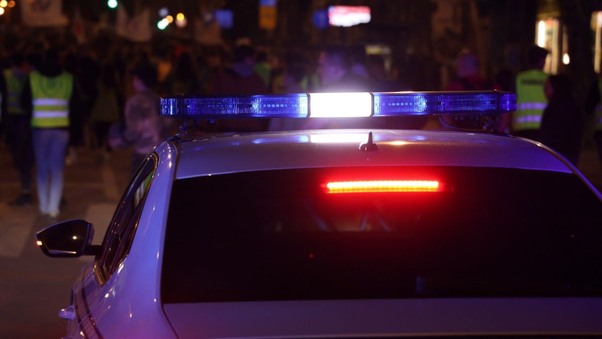 O mașină de poliție care este parcată. În fundal se văd mai mulți oameni