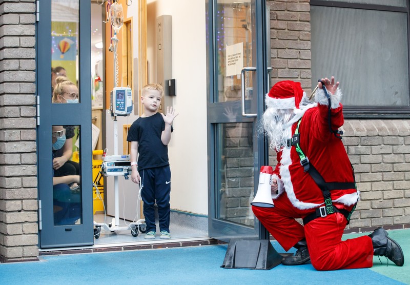 21 December 2020, England, Leeds: A man dressed as Santa Claus kneels outside an open doorway of Leeds Children's Hospital, where he visits the young patients to cheer them up before Christmas. Photo: Danny Lawson/PA Wire/dpa