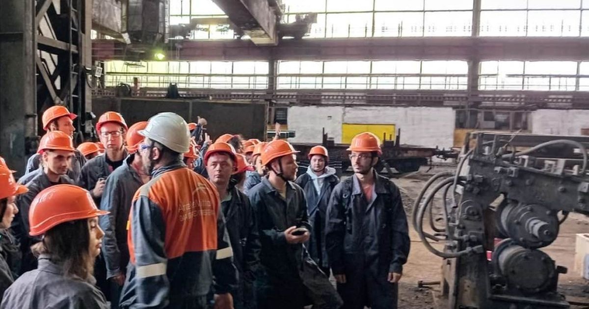 Mai mulți bărbați cu căști portocalii de protecție pe cap sunt într-o hală a combinatului ArcelorMittal Hunedoara