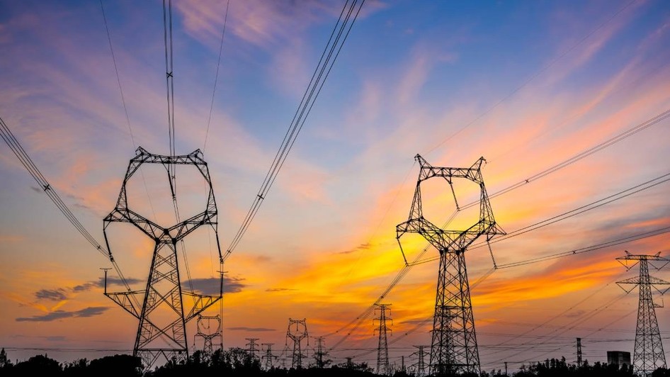 O rețea de energie cu stâlpi de curent de înaltă tensiune și cabluri interconectate, fotografiată într-o zonă de câmpie din România, la apus. Foto: Shutterstock