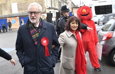 Jeremy Corbyn, alături de soția sa și de un protestatar îmbrăcat în costumul personajului Elmo, din Sesame Street, la secția de votare FOTO: EPA