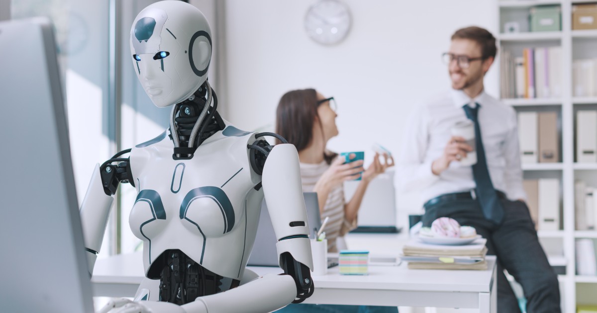 Un robot stă la un birou, în fața unui calculator și muncește. În spatele lui sunt un bărbat și o femeie, care discută între ei, sunt fericiți și beau o cafea. Bărbatul să pe biroul femeii și este îmbrpcat cu o cămașă albă, pantaloni eleganti gri și o cravată albastră la gât. Femeia stă pe un scaun, în spatele biroului său, poartă o bluză albă cu dungi negre. Amândoi poartă ochelari și țin în mână câte o ceașcă de cafea.
