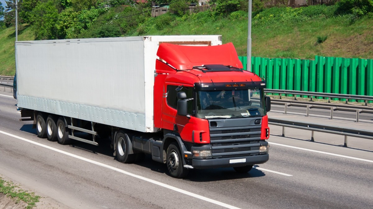 Un camion cu cabina roșie aflat în mișcare, pe autostradă