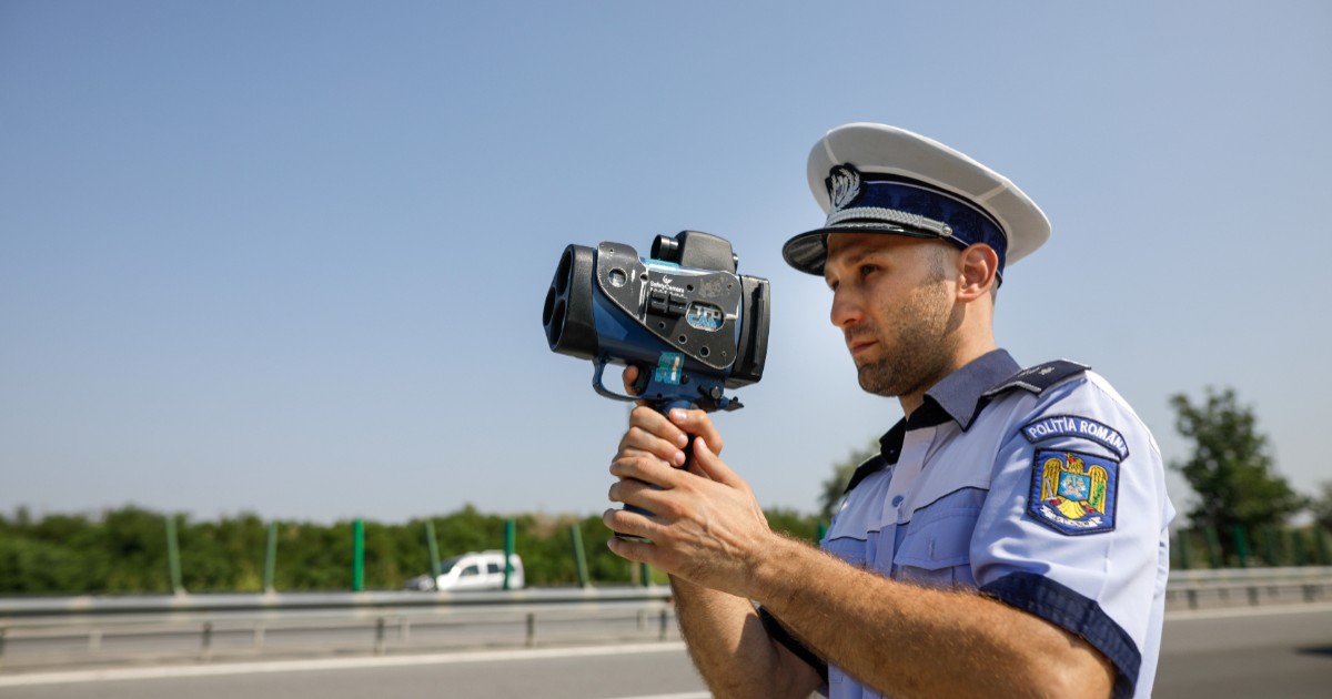 Un polițist care stă cu pistolul în mână și măsoară viteza șoferilor care merg cu mașinile și camioanele pe o autostradă din România