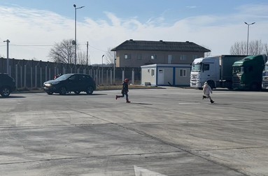 Doi copii ucraineni aleargă prin parcare