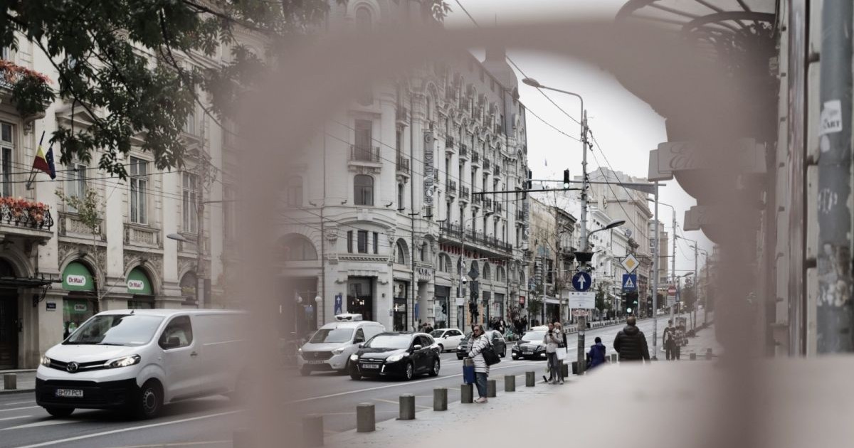 Vedere de pe bulevardul Regina Elisabeta, clădiri înalte, oameni pe stradă și mașini, văzute prin lentila aparatului foto, ce apare ca un cerc neclar, București, 27 octombrie 2025