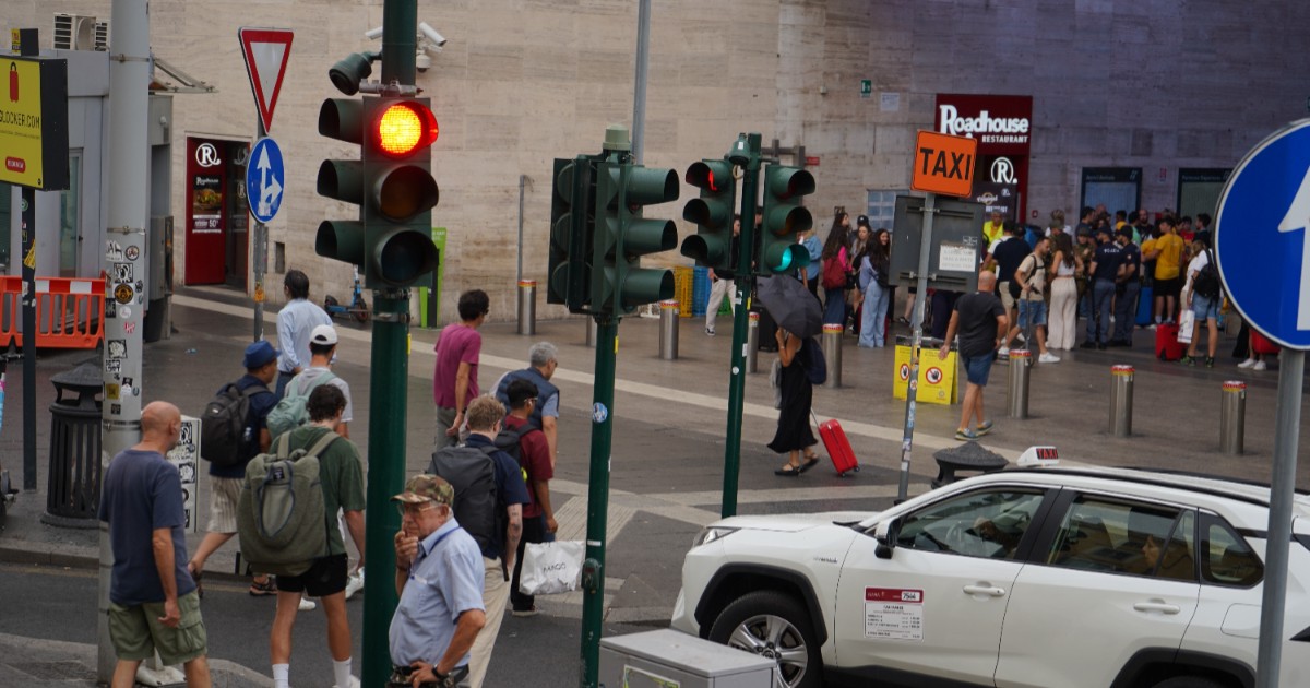Un bulevard aglomerat din Roma, Italia. Oamenii traversează pe la trecerea de pietoni, în timp ce mașinile stau la culoarea roșie a semaforului