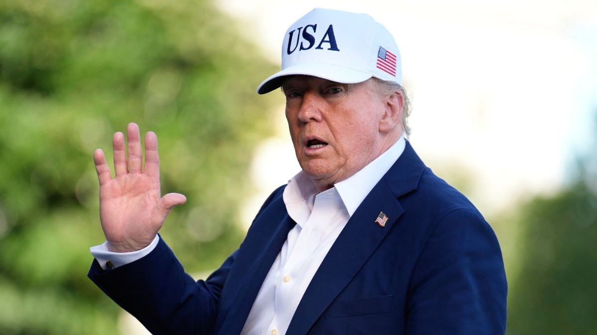 Președintele SUA, Donald Trump, in aer liber, cu o sapca alba pe cap, inscriptionata USA si steagual Americii, un sacoul inchis la culoare si o camasa albă, cu mana dreapta ridicata in semn de salut, 7 iulie 2025, CAsa Albă, Washington, DC