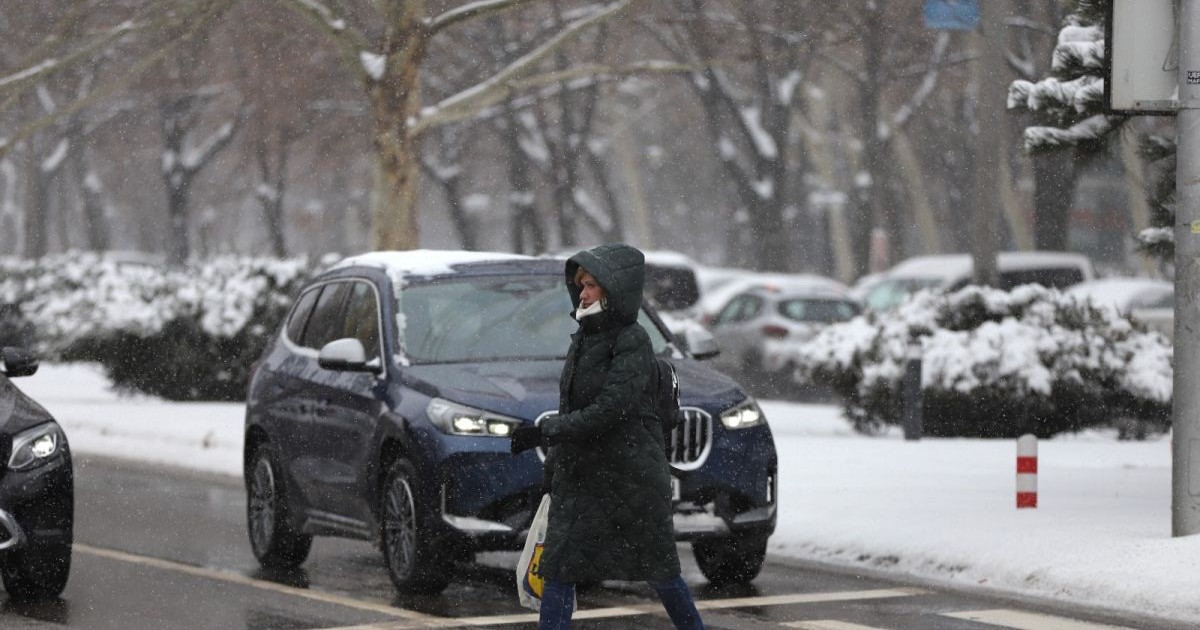 O femeie îmbrăcată cu geacă și glugă traversează strada pe trecerea de pietoni, în timp ce alte mașini au oprit, iar în jur se vede zăpadă. Foto: Libertatea/Dumitru Angelescu