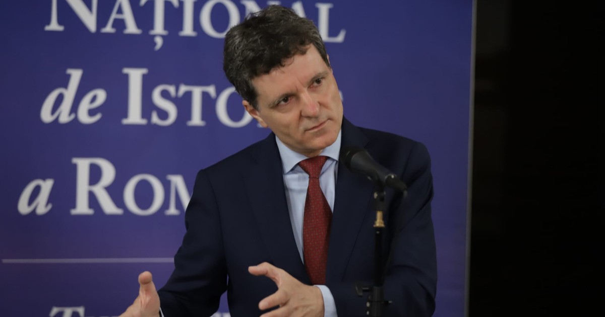 Președintele Nicușor Dan, îmbrăcat la costum și purtând o cravată roșie, gesticulează în timpul unei conferințe de presă susținută la Muzeul de Istorie