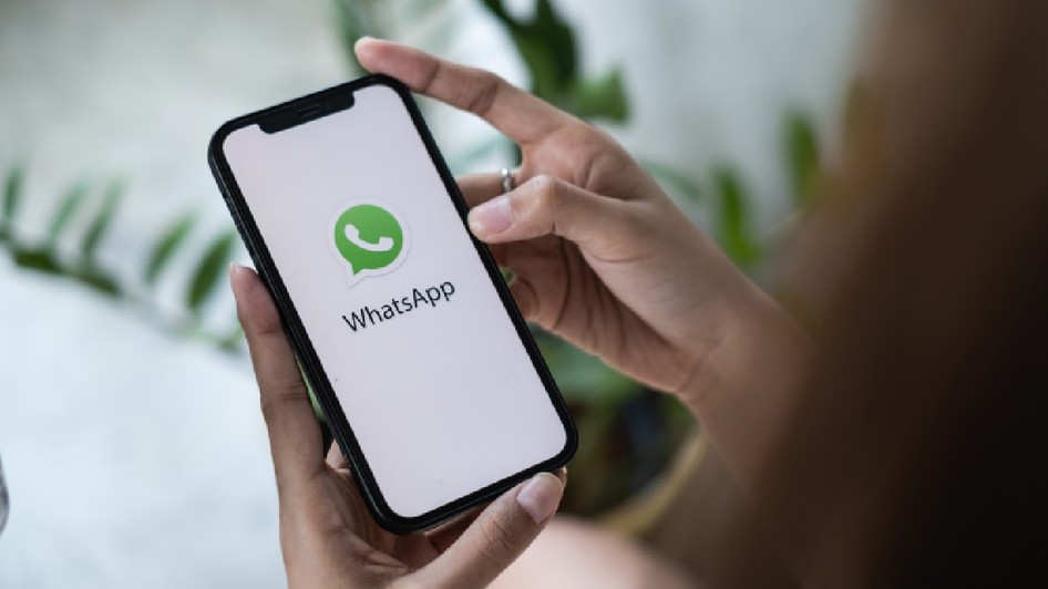 O femeie ține în mână un iPhone pe ecranul căruia este deschisă aplicația de mesagerie WhatsApp. 