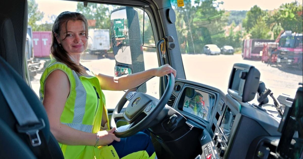 O româncă, îmbrăcată cu o vestă verde fosforescent, este la volannul unui camion de gunoi, în Germania