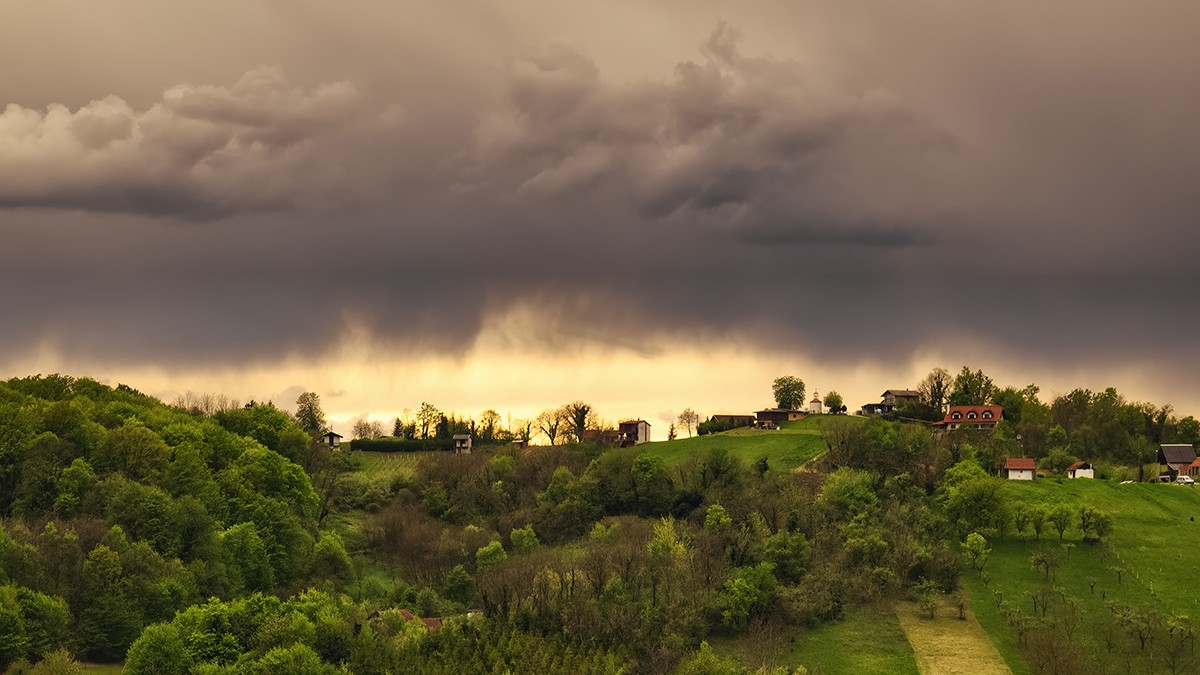 Nori negri deasupra unei localități, totul in jur fiind înconjurat de natură verde.