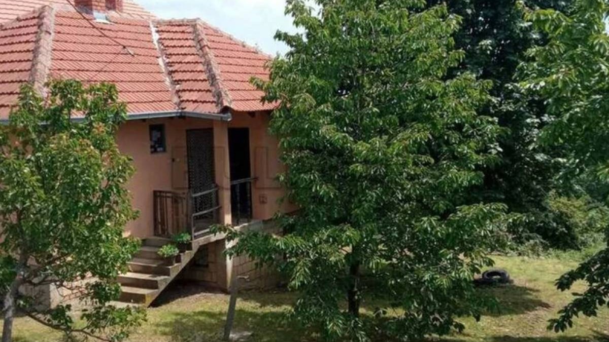 Zona rurală, Serbia - o casa cu pereti caramazii si acoperis din tigla rosie, se vad copaci mari, vetzi, langa ea