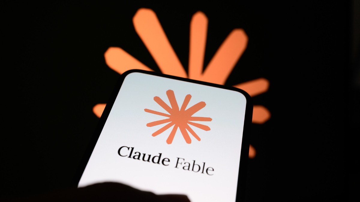 Imaginea prezintă pe ecranul unui telefon mobil logo-ul și numele Claude, chatbotul dezvoltat de compania Anthropic, pe un fundal întunecat. În spatele telefonului se observă simbolul caracteristic al platformei, evidențiat în nuanțe portocalii, sugerând tema inteligenței artificiale și a tehnologiilor digitale.
