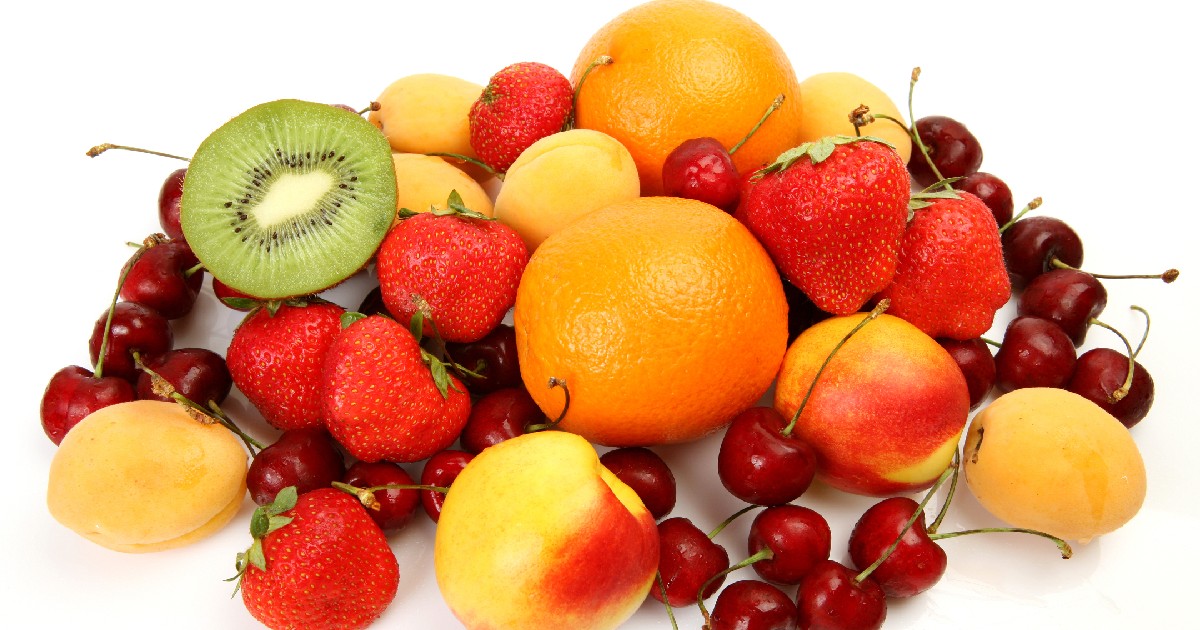 Imaginea prezintă o varietate de fructe așezate unele peste altele, pe un fundal alb. Se pot distinge mai multe tipuri de fructe proaspete: căpșuni roșii, cireșe de un roșu-închis, caise sau piersici mici, de culoare galben-portocalie, Portocale întregi,o felie de kiwi tăiată în două, care arată miezul verde și semințele negre.