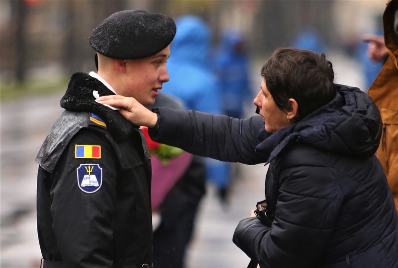 O mamă îi șterge de ploaie gulerul fiului ei, care defilează la parada militară