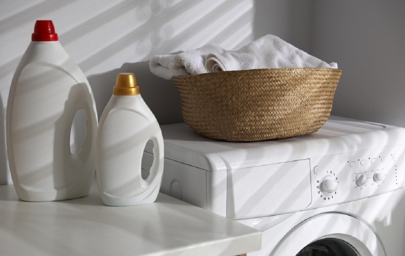 Coş de rufe pe o maşină de spălat, alături de recipiente detergent pe un blat de bucătărie