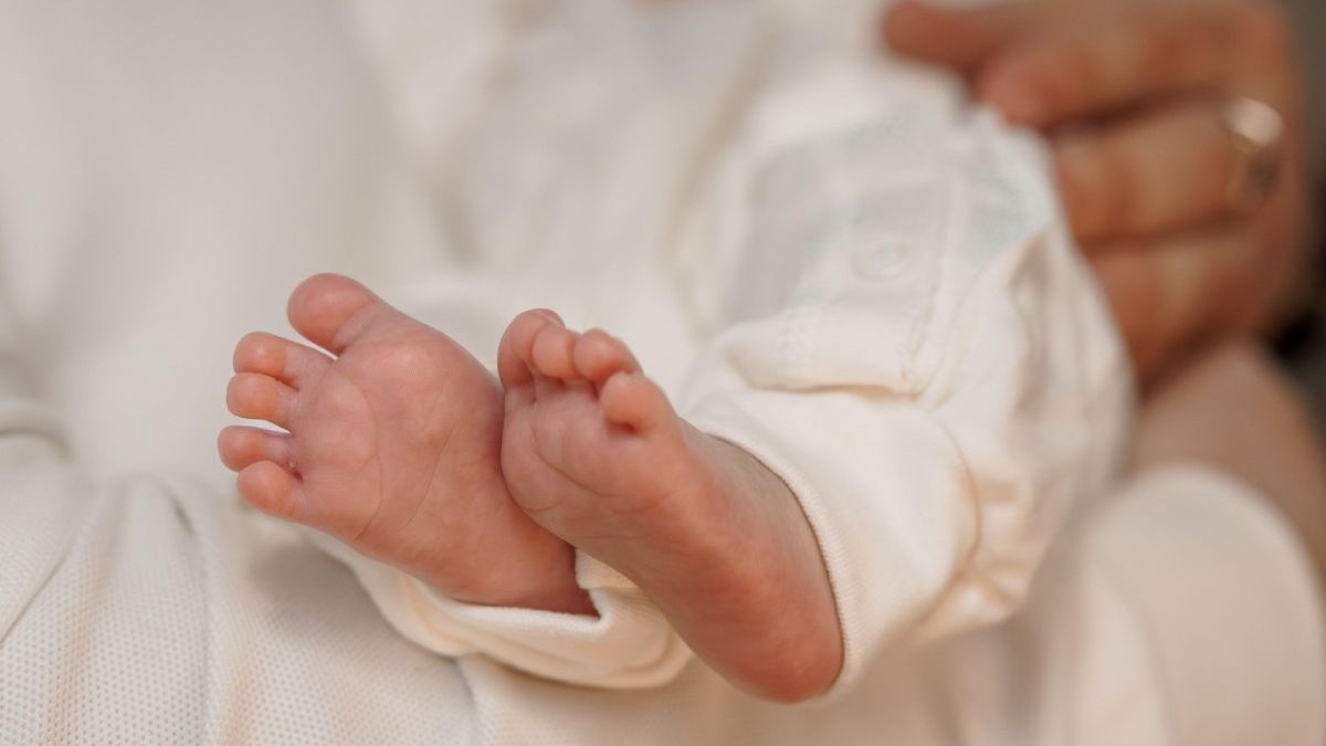 Prim-plan cu piciorușe de nou-născut ținute ușor în mâini iubitoare, înfășurate într-o pânză albă moale