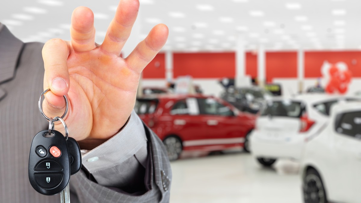 Dealer auto, barbat cu cheie auto pe care o vântură, iar în spate sunt mașinile din showroom
