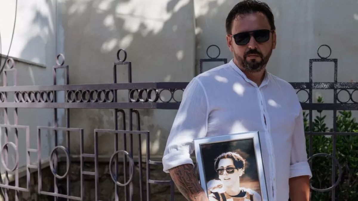 Valentin Olariu ține în mână un tablou cu portretul fiul său, Sebastian. Bărbatul are ochelari de soare la ochi și poartă o cămașă albă