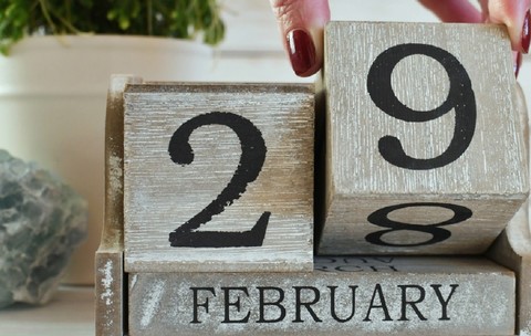 Calendar din lemn care arată data de 29 februarie, cu o mână ce mută un bloc de la 28 la 29.
