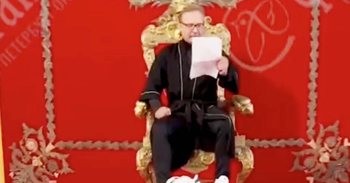 Akeksandr un bărbat îmbrăcat în negru pe un tron cu niște documente în mână.