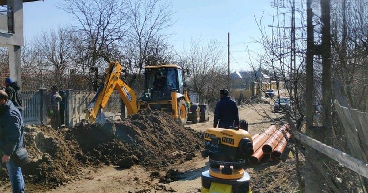 Un excavator sapă o groapă pe o stradă din comuna Cotnari pentru extinderea rețeleui de apă, mai 2024