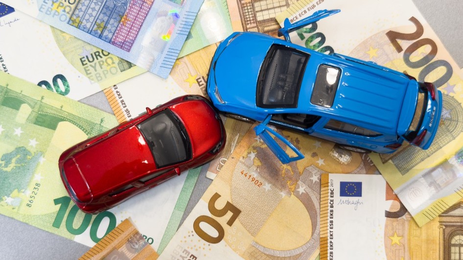 Două mașinuțe de jucărie - una roșie și una albastră - așezate deasupra unui strat de bancnote euro cu cupiuri de 50, 100 și 200 de euro.