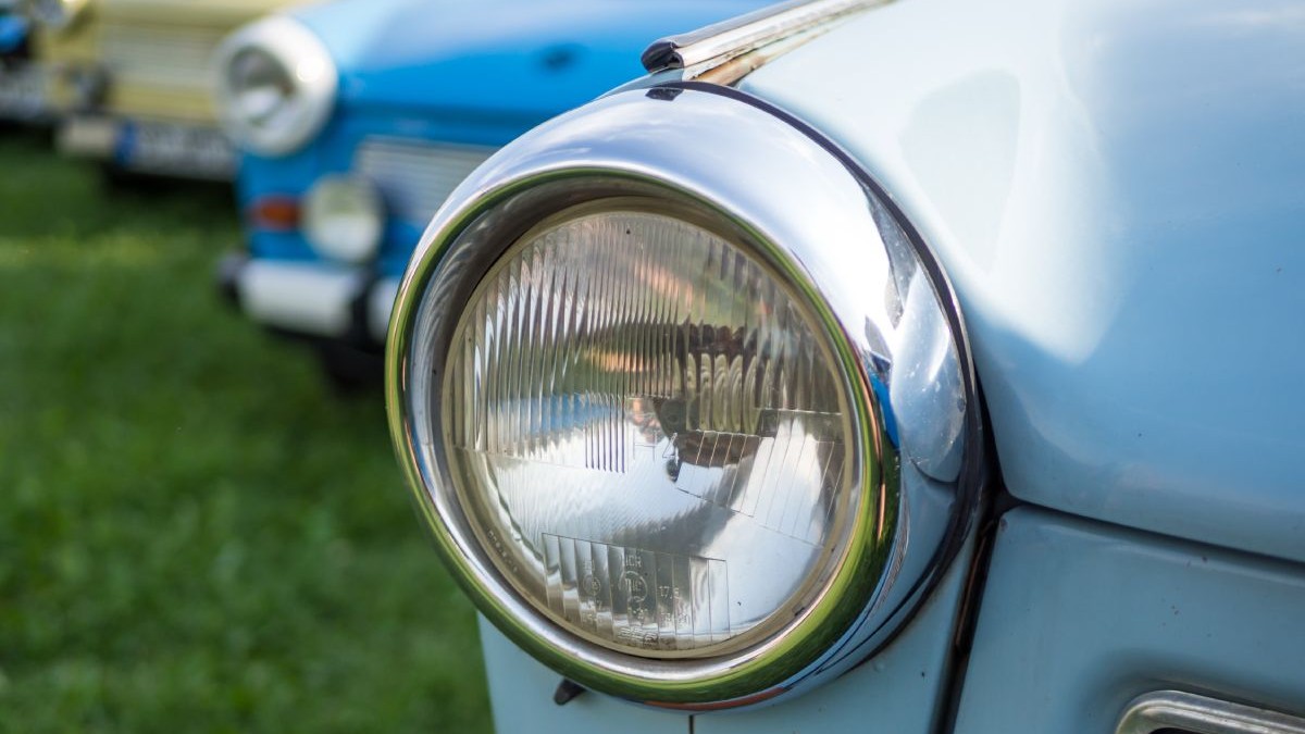 Far de Trabant, fotografiat din față, cu mașina vopsită albastru, iar pe fundal alte mașini în blur