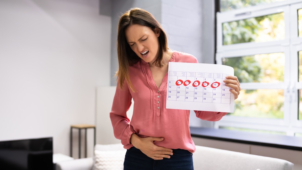Femeie care ține în mână un calendar, iar cu cealaltă își atinge burta