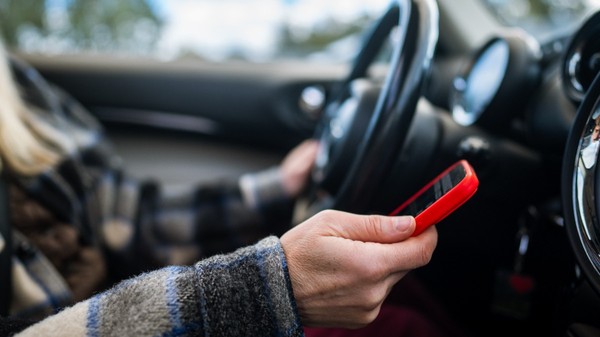 Un șofer la volan care conduce și ține un telefon în mâna dreaptă