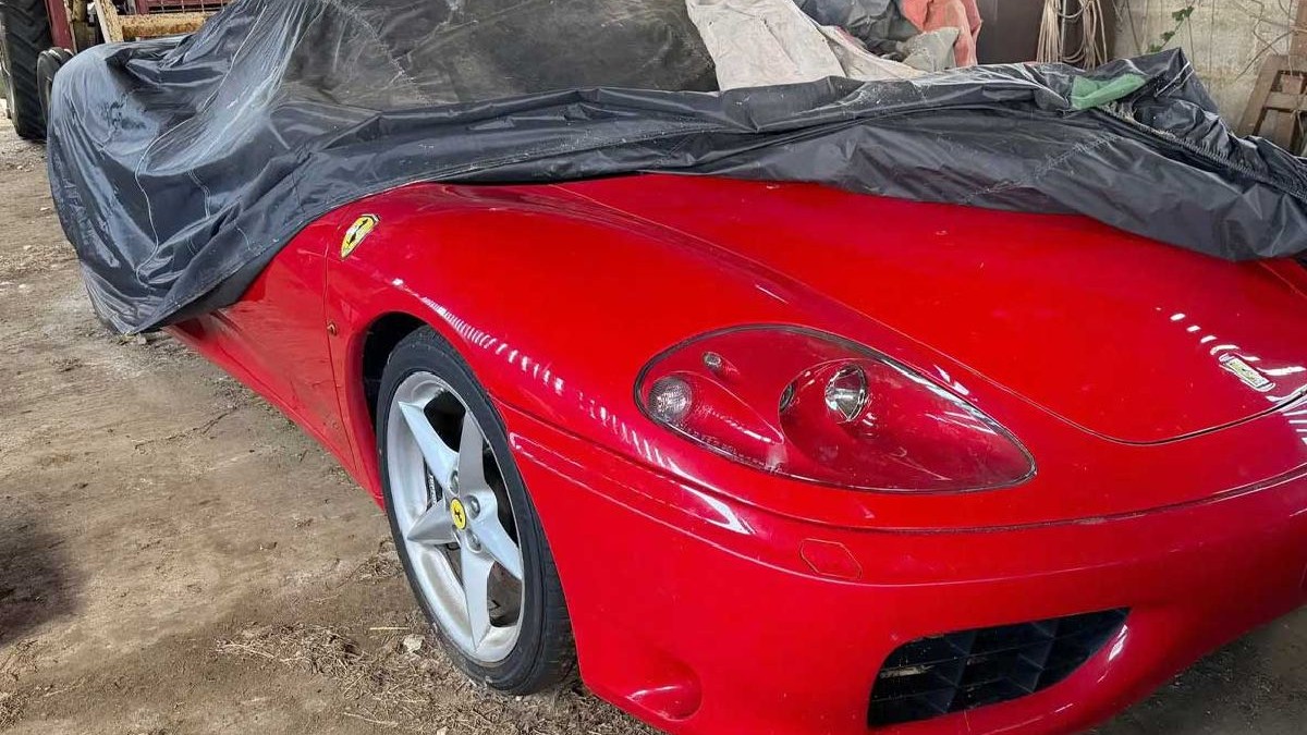 O fotografie cu un automobil sport Ferrari roșu acoperit cu o prelată neagră. Mașina are jante din aliaj argintiu cu logo-ul Ferrari.
